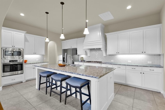 kitchen featuring a sink, custom exhaust hood, tasteful backsplash, arched walkways, and appliances with stainless steel finishes