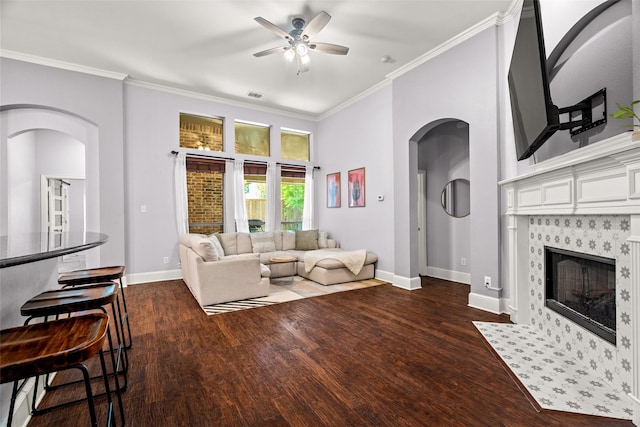 living area with dark wood-style floors, arched walkways, a ceiling fan, and ornamental molding