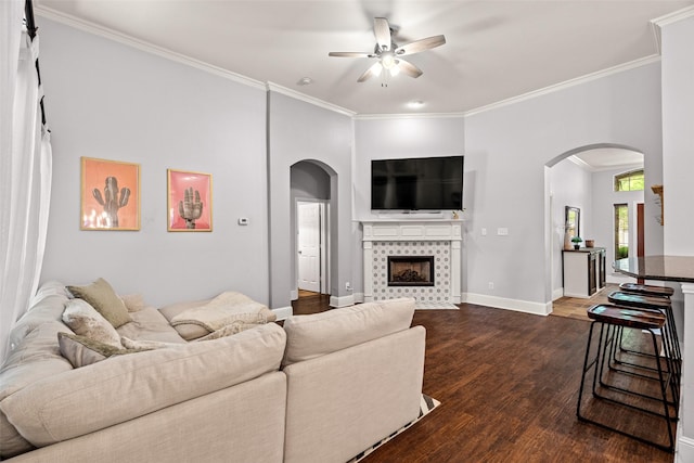 living room with dark wood-type flooring, ceiling fan, crown molding, and arched walkways