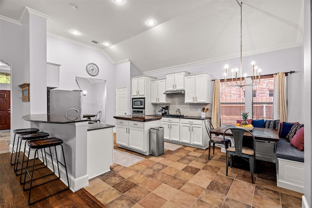 kitchen featuring crown molding, dark countertops, stainless steel appliances, a chandelier, and a peninsula