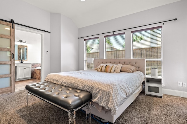 bedroom featuring lofted ceiling, connected bathroom, a sink, a barn door, and baseboards