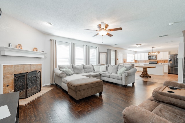 living room featuring a ceiling fan, a tiled fireplace, a textured ceiling, and a healthy amount of sunlight
