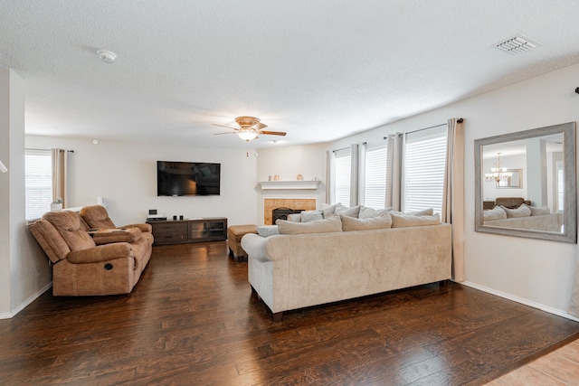 living area featuring visible vents, baseboards, a fireplace, dark wood-type flooring, and ceiling fan with notable chandelier