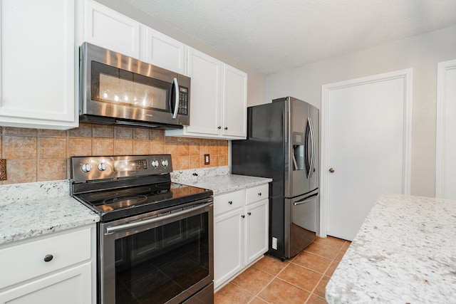 kitchen featuring light tile patterned floors, white cabinets, stainless steel appliances, and decorative backsplash
