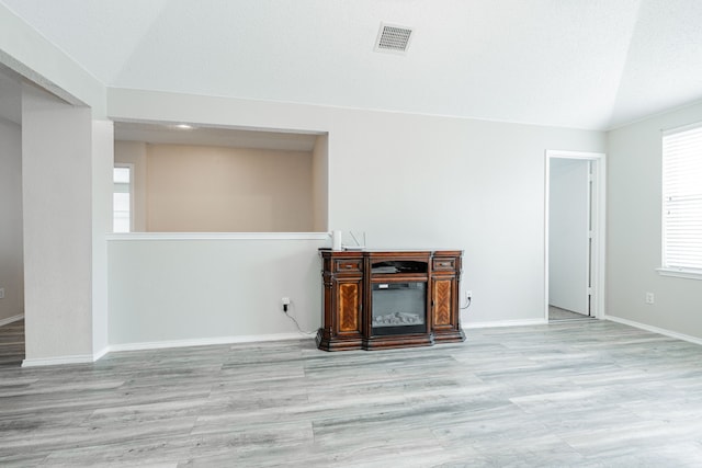 unfurnished living room with baseboards, visible vents, wood finished floors, and lofted ceiling
