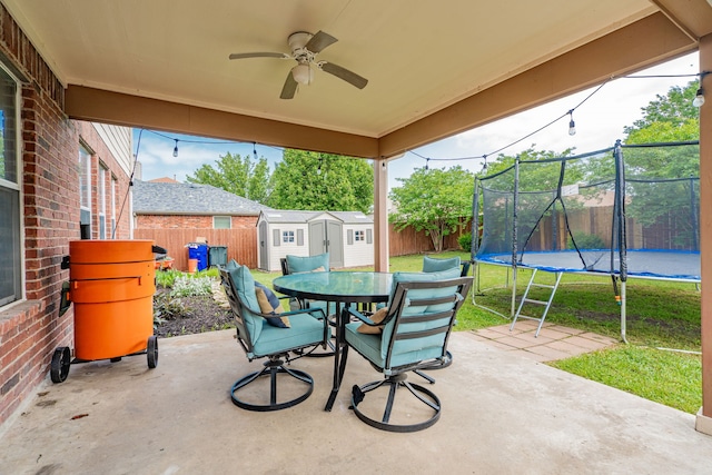 view of patio featuring outdoor dining area, a trampoline, a storage unit, and a fenced backyard