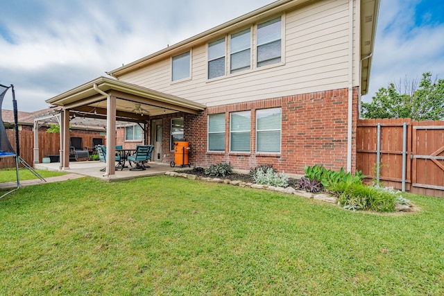 back of house featuring a trampoline, brick siding, a fenced backyard, and a patio area