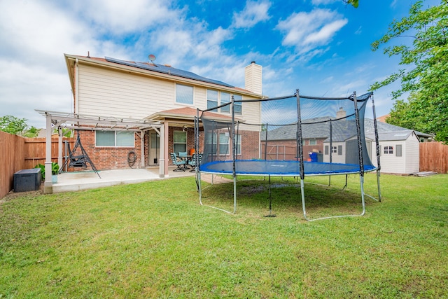 rear view of house featuring a patio, a pergola, a trampoline, roof mounted solar panels, and a storage unit