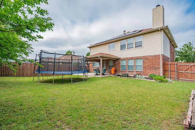 back of property featuring a trampoline, a patio area, a yard, a chimney, and brick siding