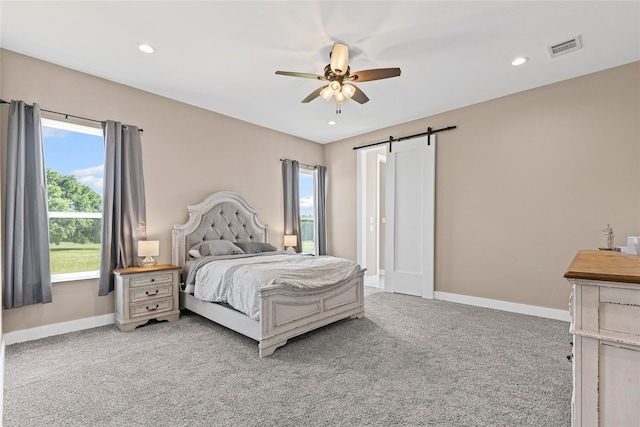 carpeted bedroom featuring multiple windows, visible vents, baseboards, and a barn door