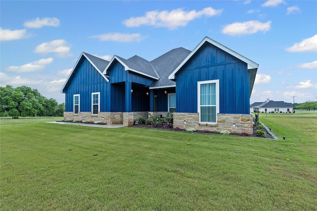 view of front of house featuring a shingled roof, board and batten siding, a front lawn, and stone siding