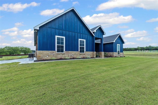 view of front of house featuring board and batten siding, central AC unit, a front yard, and stone siding