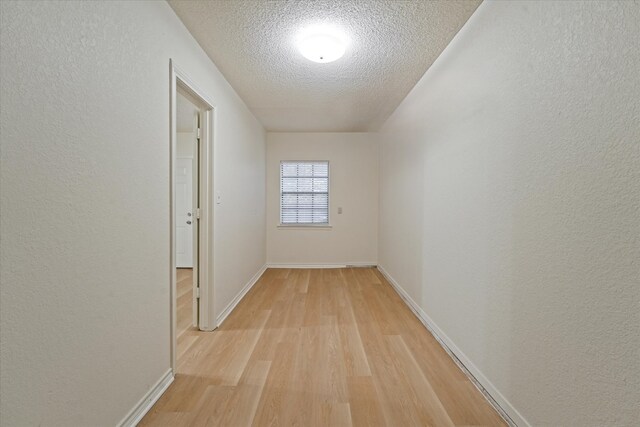 hall featuring a textured ceiling, a textured wall, baseboards, and light wood-style floors