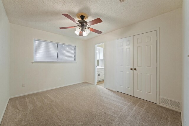 unfurnished bedroom featuring visible vents, a closet, light colored carpet, connected bathroom, and a textured ceiling