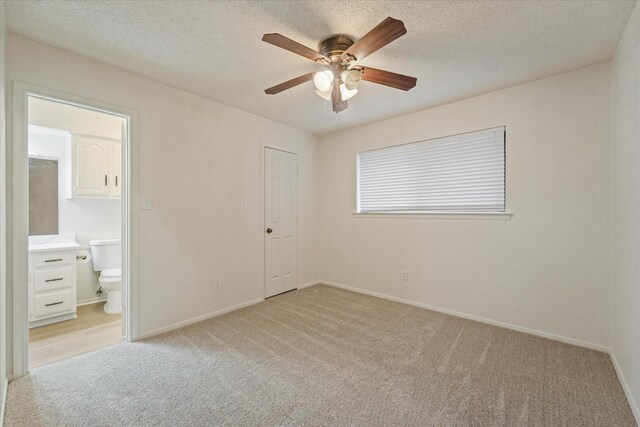 unfurnished bedroom with baseboards, light colored carpet, connected bathroom, a textured ceiling, and a ceiling fan