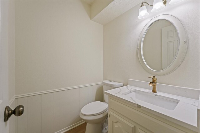 half bath with vanity, wainscoting, and toilet