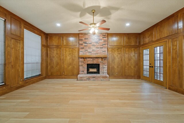unfurnished living room featuring wooden walls, a ceiling fan, french doors, and light wood-type flooring