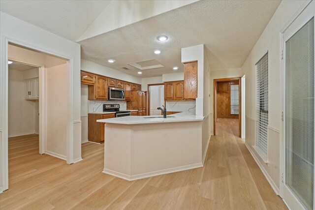 kitchen with brown cabinets, a sink, a textured ceiling, stainless steel appliances, and light wood-type flooring