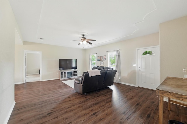 living area with dark wood-type flooring, a ceiling fan, and baseboards