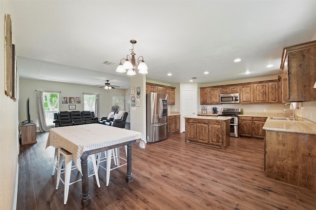 kitchen with brown cabinets, a sink, appliances with stainless steel finishes, dark wood-style floors, and a center island
