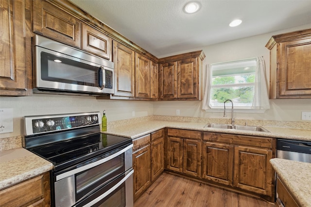 kitchen with wood finished floors, brown cabinetry, appliances with stainless steel finishes, light countertops, and a sink