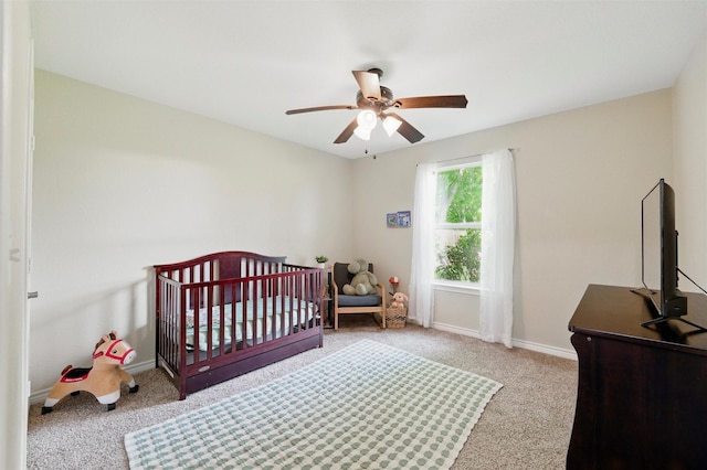 carpeted bedroom with ceiling fan, a crib, and baseboards
