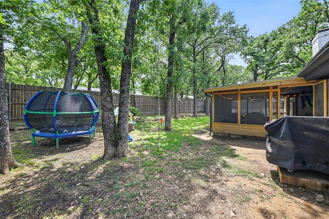 view of yard featuring a fenced backyard, a trampoline, and a sunroom