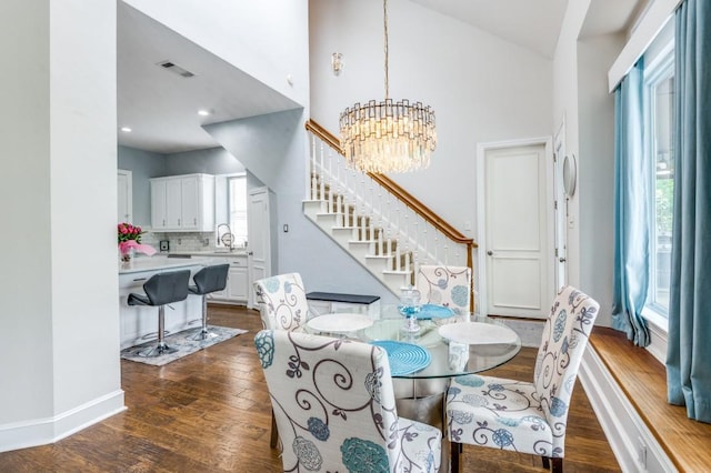 dining area featuring dark wood-style flooring, a notable chandelier, high vaulted ceiling, stairs, and visible vents