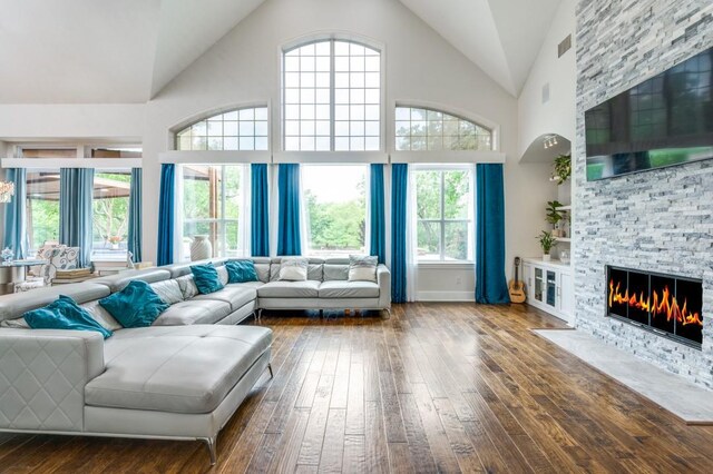 living area with wood-type flooring, high vaulted ceiling, visible vents, and a stone fireplace