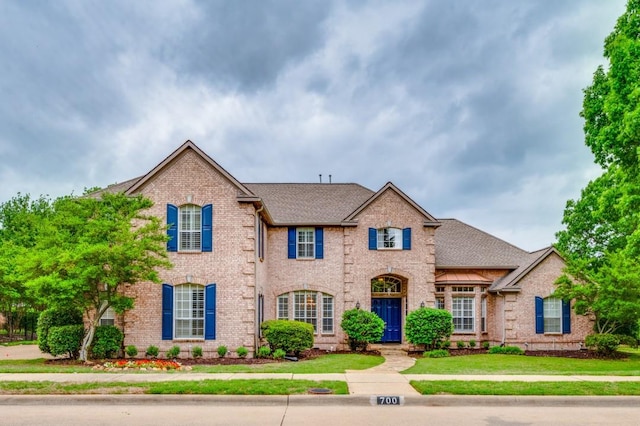 traditional home featuring brick siding, roof with shingles, and a front yard