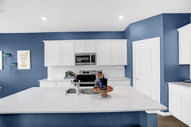 kitchen featuring white cabinets, light stone counters, a sink, appliances with stainless steel finishes, and backsplash