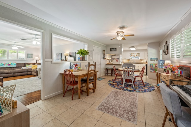 dining space featuring crown molding, wainscoting, ceiling fan, and light tile patterned floors