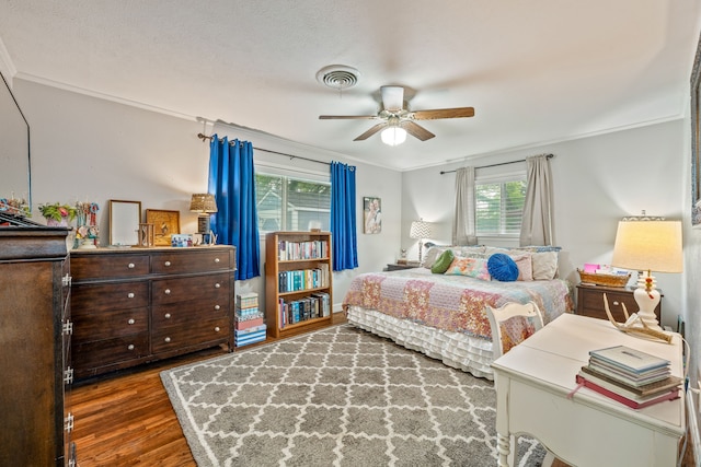 bedroom with a ceiling fan, visible vents, ornamental molding, and wood finished floors