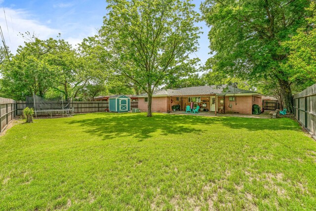 view of yard with a fenced backyard, a trampoline, an outbuilding, and a storage shed