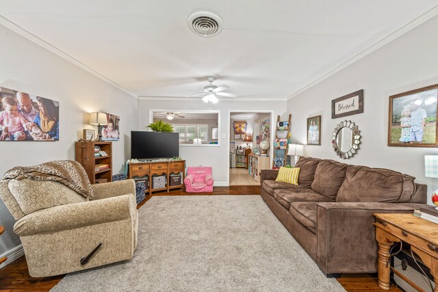living room with visible vents, ornamental molding, wood finished floors, baseboards, and ceiling fan