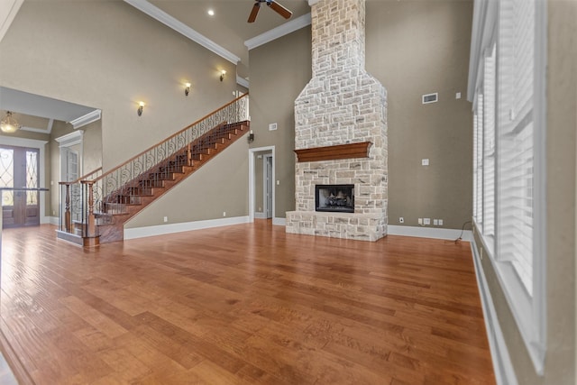 unfurnished living room featuring a ceiling fan, a towering ceiling, stairway, baseboards, and ornamental molding