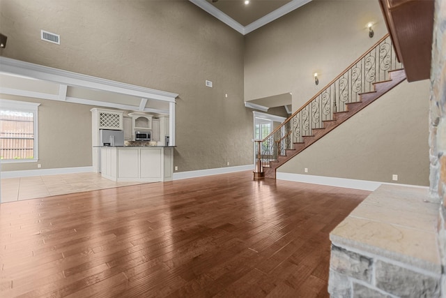 unfurnished living room featuring visible vents, baseboards, crown molding, and light wood-type flooring