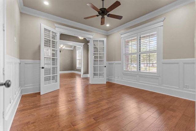 spare room featuring wainscoting, ornamental molding, french doors, and ceiling fan with notable chandelier