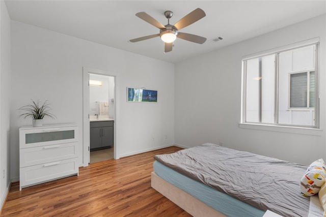 bedroom featuring wood finished floors, ensuite bath, a sink, baseboards, and visible vents