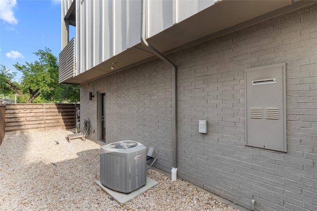 view of side of property featuring brick siding, fence, board and batten siding, and central AC unit