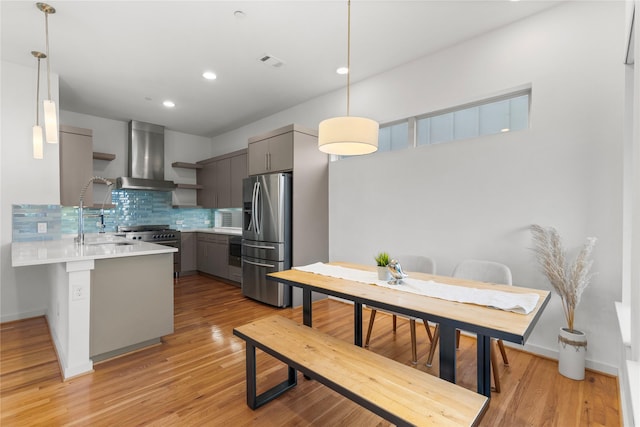 kitchen with wall chimney range hood, decorative backsplash, appliances with stainless steel finishes, a peninsula, and gray cabinets