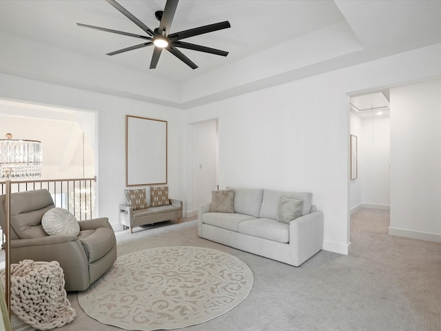 living area with a ceiling fan, attic access, light colored carpet, baseboards, and a tray ceiling