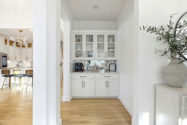 bar with decorative backsplash, refrigerator, baseboards, light wood finished floors, and an inviting chandelier