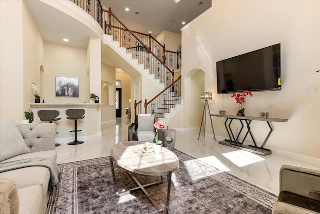living area with a high ceiling, stairs, marble finish floor, baseboards, and arched walkways