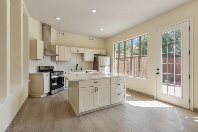 kitchen with a sink, stainless steel appliances, light wood-type flooring, wall chimney exhaust hood, and visible vents