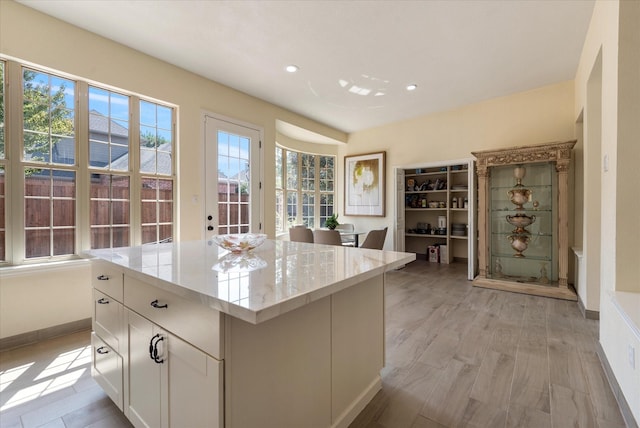 interior space with recessed lighting, light stone countertops, a center island, baseboards, and white cabinets