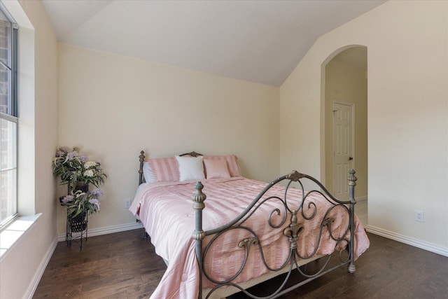 bedroom featuring dark wood-style floors, arched walkways, vaulted ceiling, and baseboards