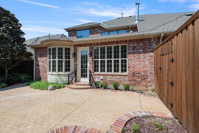 back of house featuring a patio, fence, roof with shingles, and brick siding
