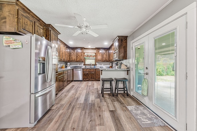 kitchen with a ceiling fan, a textured ceiling, light wood-style flooring, and appliances with stainless steel finishes