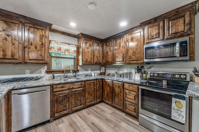kitchen featuring a sink, light wood-style floors, a textured ceiling, stone countertops, and stainless steel appliances